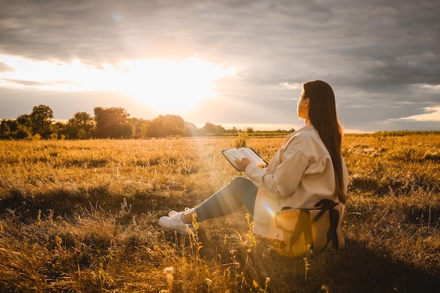 A mulher cristã segura a bíblia nas mãos lendo a bíblia sagrada em um campo durante o belo pôr do sol conceito de fé, espiritualidade e religião esperança de paz