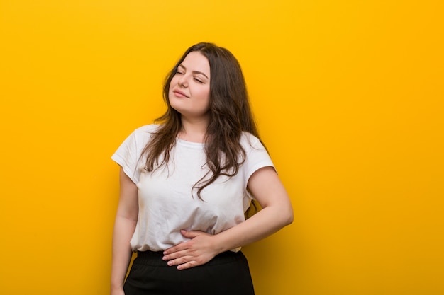 A mulher curvy nova mais do tamanho toca na barriga, sorri delicadamente, comendo e conceito da satisfação.