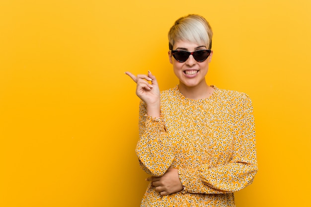 A mulher curvy nova que desgasta um verão floral veste o sorriso que aponta alegremente com dedo indicador afastado.