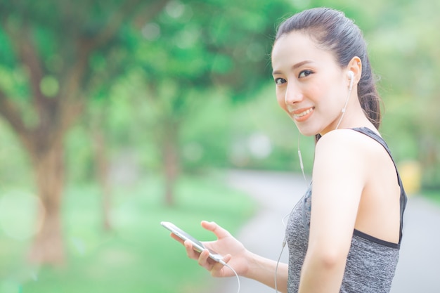 A mulher da aptidão está escutando a música de seu telefone celular ao correr no parque.