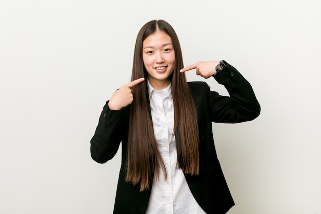 A mulher de negócio consideravelmente chinesa dos jovens sorri, apontando os dedos na boca.