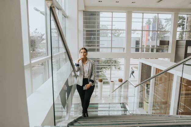 Foto a mulher de negócio nova está nas escadas no escritório e usa o telefone móvel