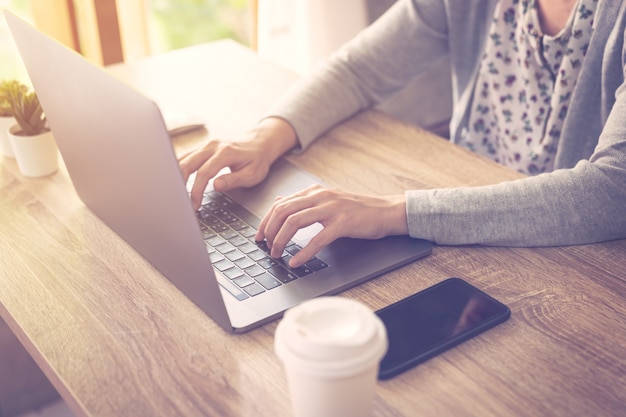 A mulher de negócio que usa o laptop faz a atividade em linha no escritório de madeira da tabela no escritório home.