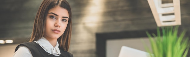 A mulher de negócios com um laptop sentada na frente da mesa