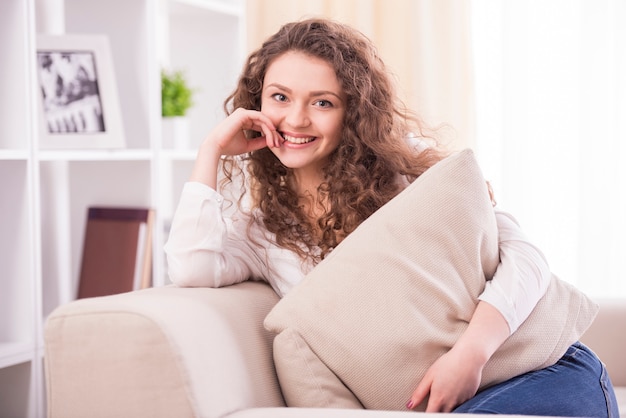 A mulher de sorriso nova está sentando-se em um sofá em casa.