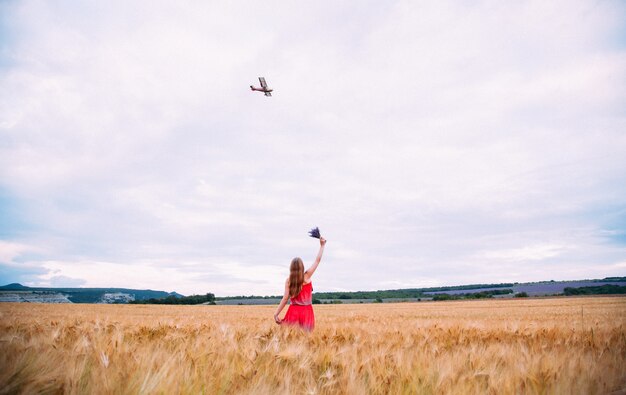 A mulher de vestido vermelho no campo de trigo, acenando para o avião.