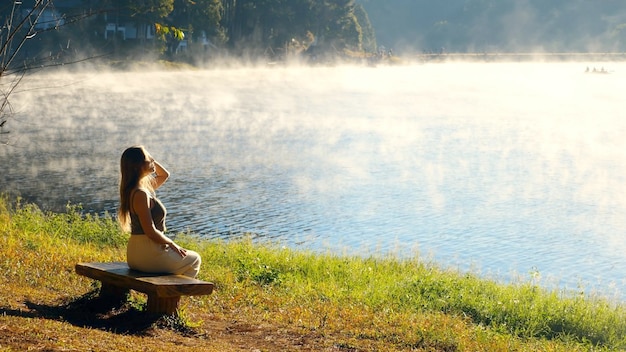 A mulher de viagem relaxa na natureza perto da viajante feminina do lago enevoado sentada no banco