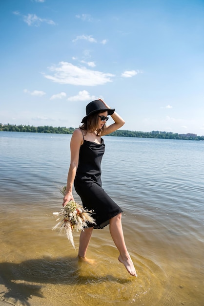 A mulher descalça anda na lagoa no dia de verão do vestido preto