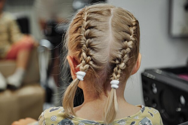 A mulher do barbeiro faz um penteado bonito na moda para uma menina loira bonitinha na barbearia moderna, salão de cabeleireiro. cabeleireiro faz penteado para bebê na barbearia. penteado e beleza do conceito