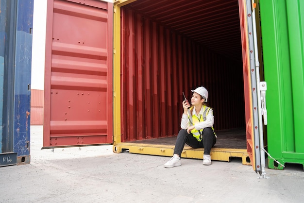 Foto a mulher do capataz sorria sentada dentro do contêiner de carga no armazém gerente supervisor de segurança no conceito de porta do terminal personalizado de contêiner importação exportação