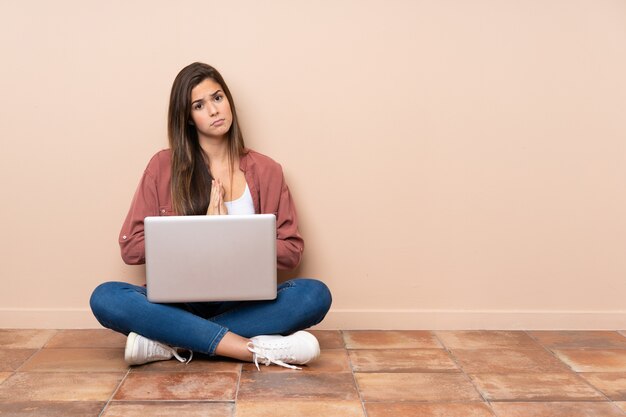 A mulher do estudante adolescente sentada no chão com um laptop mantém a palma da mão unida. pessoa pede algo