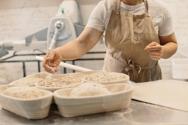 A mulher do padeiro polvilha farinha nos pães em forma de pão de estilo rústico antes de assar pão rústico de grãos inteiros