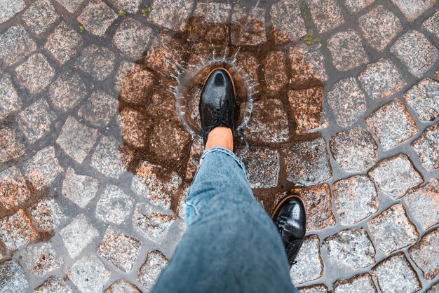 A mulher do ponto de vista da primeira pessoa entra na poça de sapatos pretos, o outono está chegando