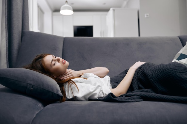 A mulher encontra-se em casa no sofá coberta com problemas de saúde cobertores