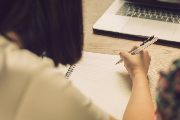 A mulher escreve no caderno com o portátil na tabela no café.