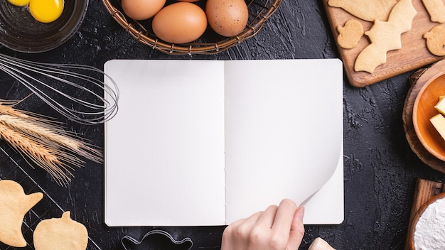 A mulher está lendo a receita do livro de receitas de fazer biscoitos de halloween com o conceito de design de ingredientes de cozimento da vista superior da aula de culinária sobre a cabeça