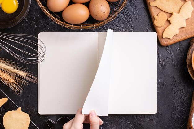 Foto a mulher está lendo a receita do livro de receitas de fazer biscoitos de halloween com o conceito de design de ingredientes de cozimento da vista superior da aula de culinária sobre a cabeça