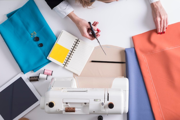 A mulher está prestes a cortar o material vermelho com uma tesoura