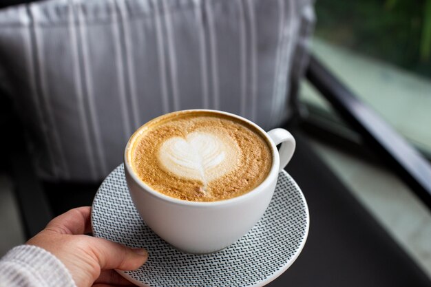 A mulher está segurando a xícara de cappuccino quente no café Latte art em forma de coração para o símbolo do amor