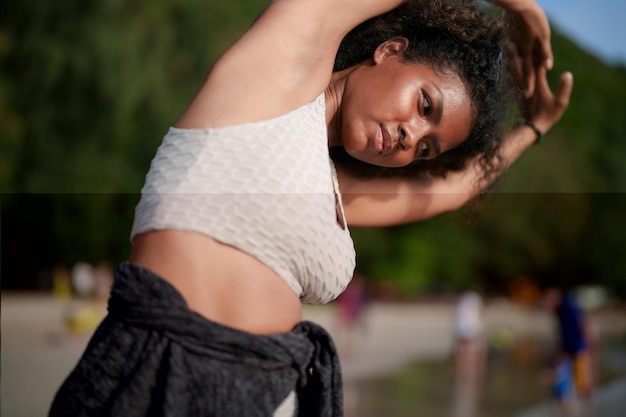 A mulher exercita e estica os músculos antes do treino ao ar livre Retrato sexy senhora africana asiática preparando-se para fitness na praia