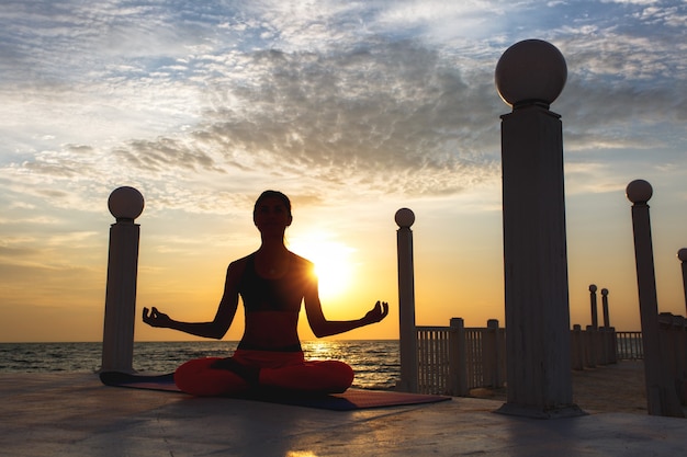 A mulher fazendo ioga ao nascer do sol perto do mar