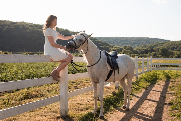 A mulher feliz está acariciando um cavalo enquanto está sentado em cima do muro