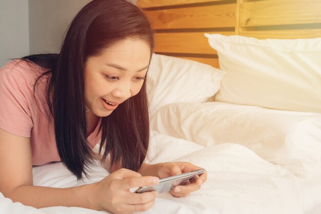 A mulher feliz está jogando o jogo móvel em sua cama.