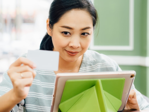 A mulher feliz está usando um cartão de crédito branco do modelo para a compra em linha na tabuleta.