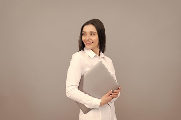 A mulher feliz na camisa branca segura a nova tecnologia do computador