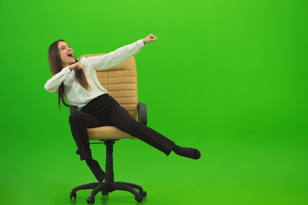Foto a mulher feliz se divertindo na cadeira sobre o fundo verde