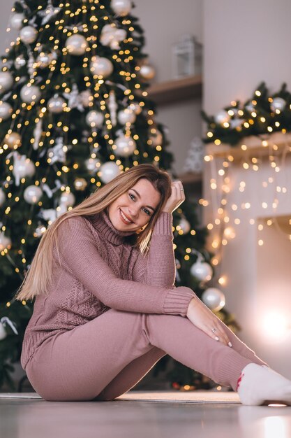 A mulher feliz senta-se junto à lareira perto da decoração da árvore de Natal