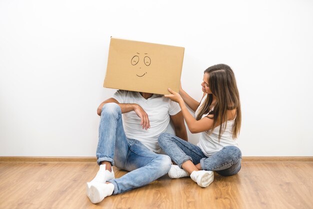 A mulher feliz sentada perto do homem com uma caixa de papelão na cabeça