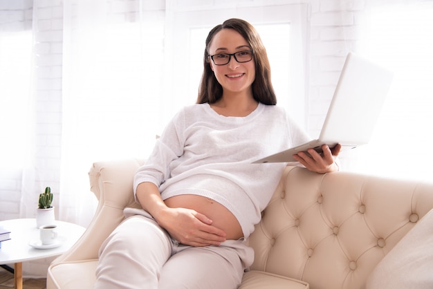 A mulher gravida está datilografando no computador portátil.