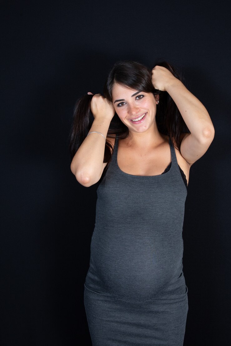 Foto a mulher gravida feliz bonita no vestido cinzento joga o cabelo