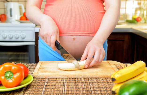 A mulher gravida prepara uma banana na cozinha