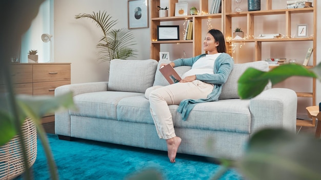 A mulher grávida relaxa e lê o livro no sofá em casa pensando ou contemplando a ideia de gravidez e a mulher sentada no sofá estudando literatura, história de fantasia ou romance no salão da casa sozinha