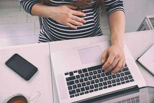 A mulher grávida trabalhando com laptop