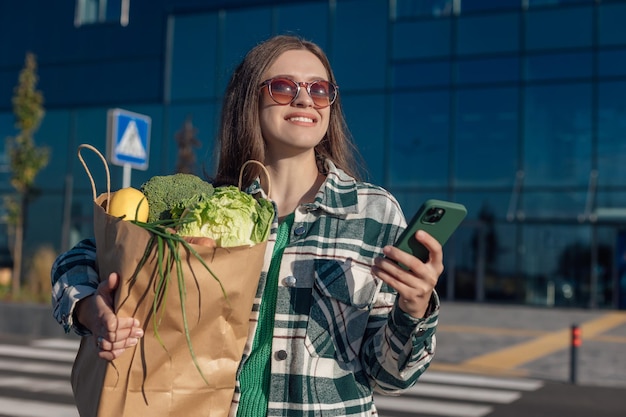 A mulher guarda o smartphone e o saco de compras com mantimentos nas mãos