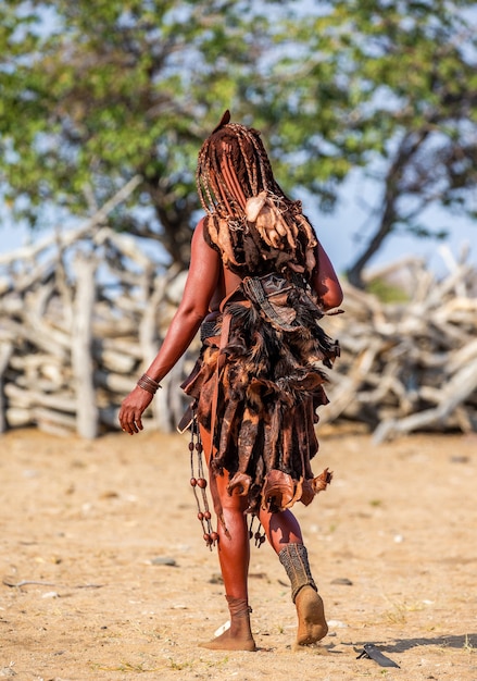 A mulher Himba em trajes tradicionais caminha pelo deserto.