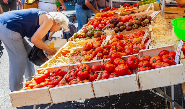 A mulher idosa escolhe e compra um tomate no mercado