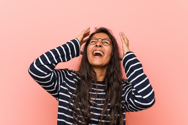 A mulher indiana intelectual nova ri alegremente mantendo as mãos na cabeça. Conceito de felicidade.