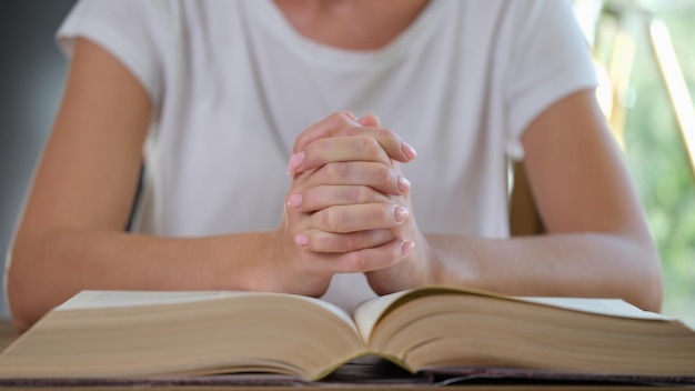 A mulher lê um livro grosso e reza fechando as mãos femininas conectadas na esperança da religião do livro aberto e