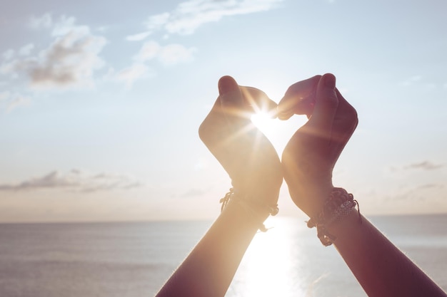 A mulher levanta as mãos para o céu em forma de coração ao redor do sol