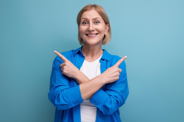 A mulher madura mostra suas mãos em direções diferentes em um fundo azul com copyspace