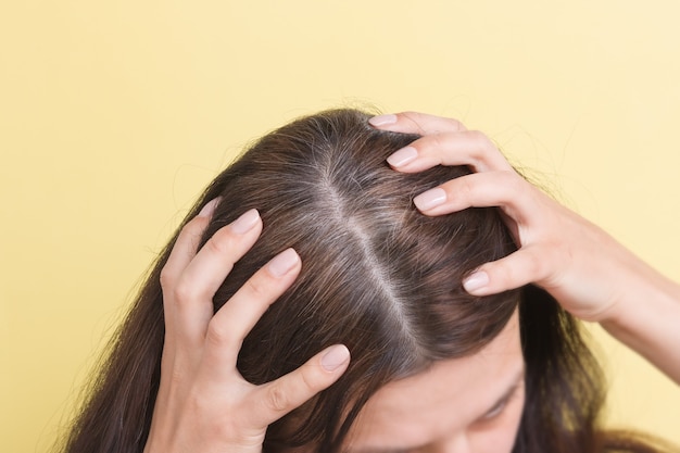 A mulher mostra cabelos grisalhos na cabeça. cabelo com fragmentos de cabelo grisalho requerendo coloração em um fundo amarelo