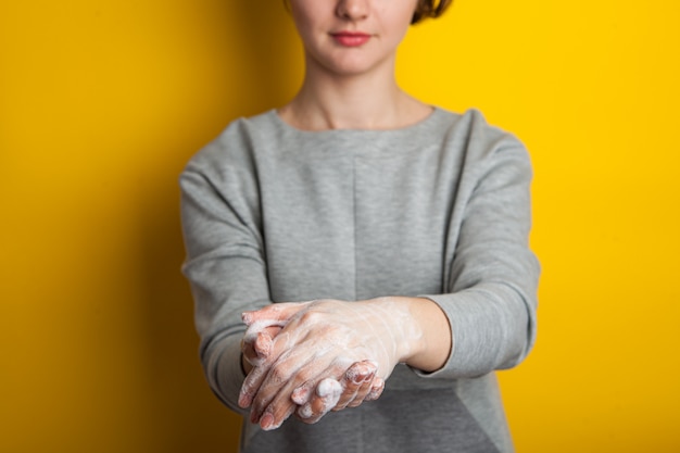 A mulher mostra como ensaboar as mãos com sabão. parede brilhante amarela, isolada. desinfecção das mãos para prevenir a doença de coronavírus.