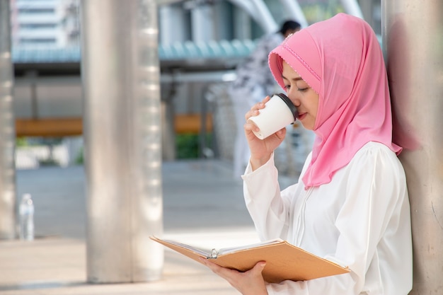A mulher muçulmana está bebendo a bebida quente ao ler o livro.