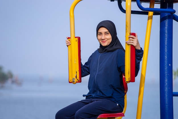 A mulher muçulmana que veste a roupa e o hijab escuros cobre seus exercícios do cabelo no peso corporal.