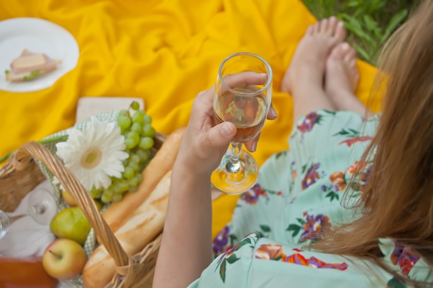 A mulher no piquenique senta-se na tampa amarela e guarda o vidro de vinho.