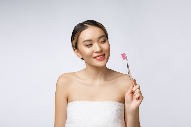 A mulher nova bonita no fundo isolado branco prende uma escova de dentes, asiática